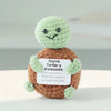 Handmade crochet potato doll with a green head and brown body holding an inspirational card