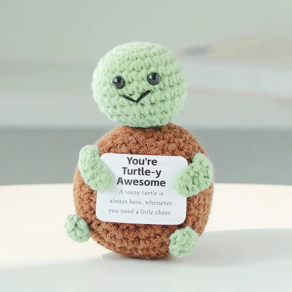 Handmade crochet potato doll with a green head and brown body holding an inspirational card