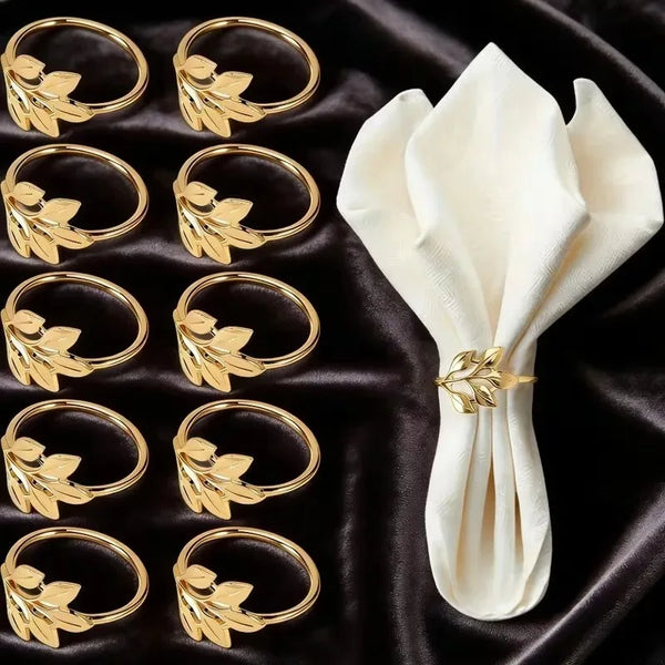 A set of gold alloy napkin rings with leaf designs displayed on a dark fabric.