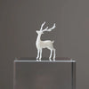 A white resin ornament of an elk deer with antlers standing on a clear glass block.