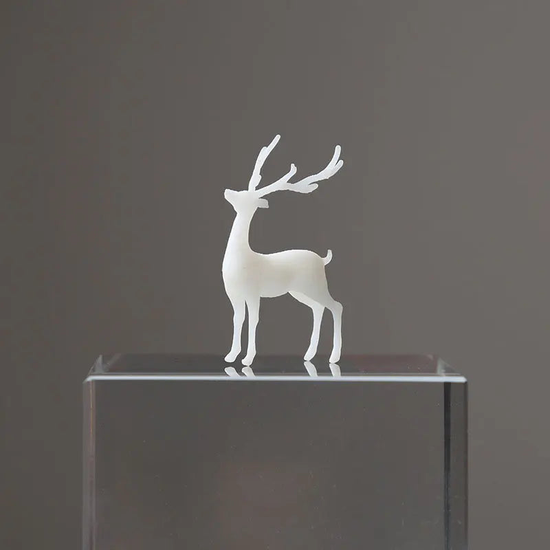 A white resin ornament of an elk deer with antlers standing on a clear glass block.