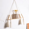 A rustic wooden wall shelf with macrame hangers displaying dried yellow flowers and white tassels.