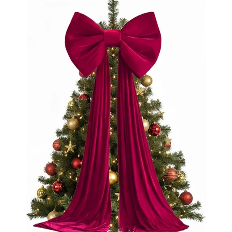A Christmas tree decorated with gold ornaments and a large red velvet bow and long streamers.