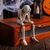 Three white resin skeleton skull figurines are displayed on a wooden box with long legs.