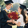 A smiling graduate in a black gown and cap is handing a bouquet of red glitter artificial roses to a female student.