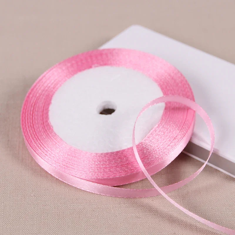 Pink satin ribbon spool with a loose ribbon unwound on a white background