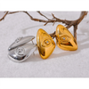 A pair of geometric stud earrings in silver and gold tones resting on a white surface with dry branches.