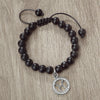 A handmade beaded bracelet with natural black stones and a silver zodiac charm on a neutral background.