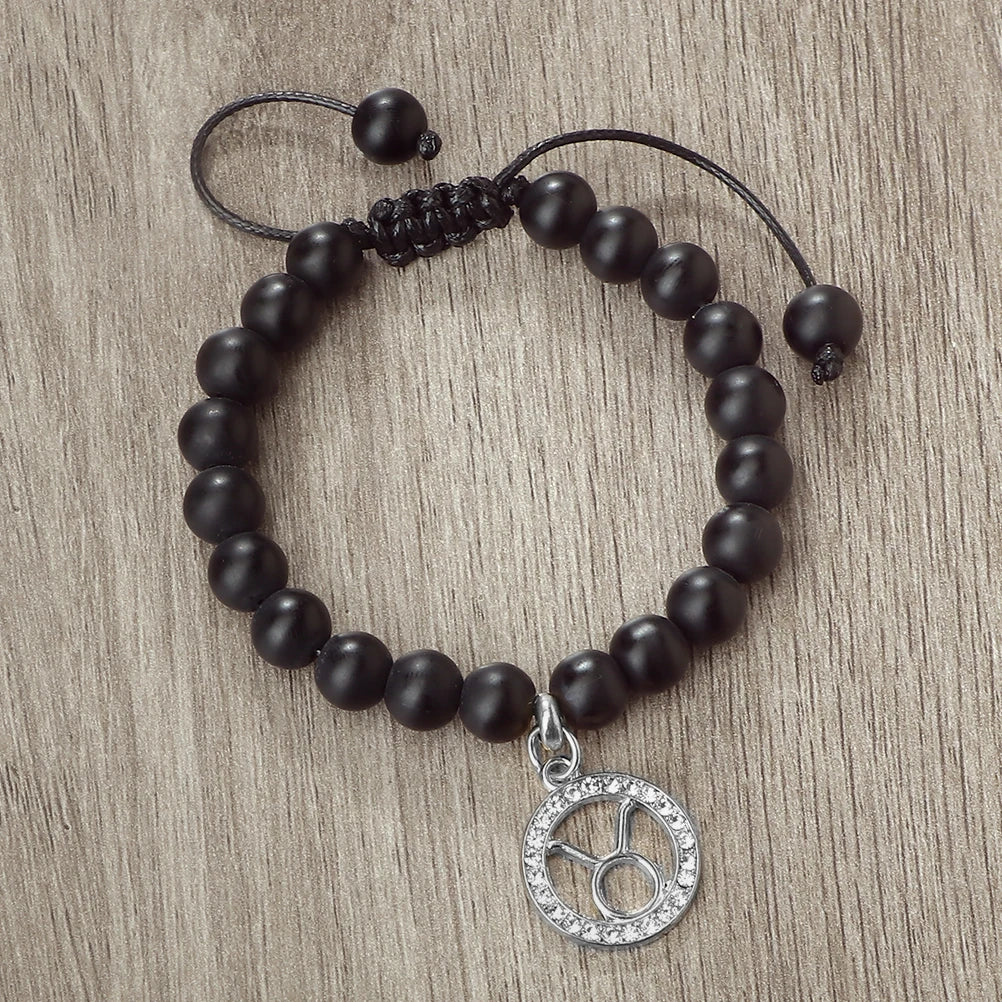 A handmade beaded bracelet with natural black stones and a silver zodiac charm on a neutral background.