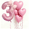 Pink foil balloons shaped like the number three and hearts for party decoration