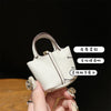 A close-up of a small, cream-colored leather handbag with a wrist strap, held by a hand.