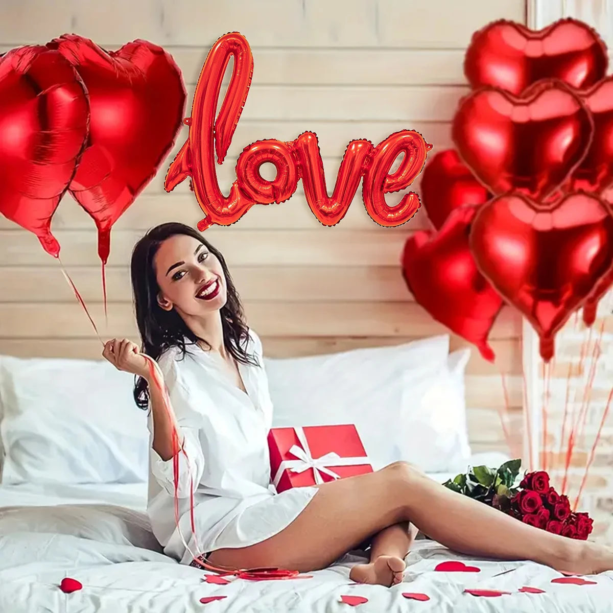 Eine lächelnde Frau liegt im Bett umgeben von roten Herzballons und Blütenblättern