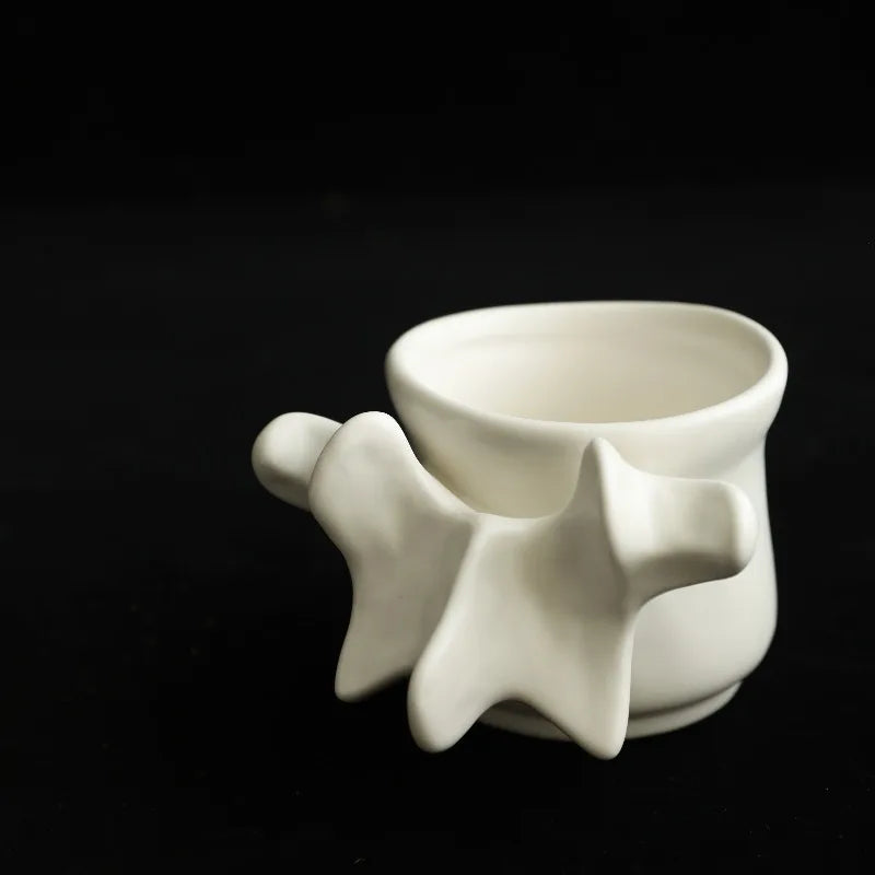 A white ceramic vase shaped like a vertebra, photographed against a black background.