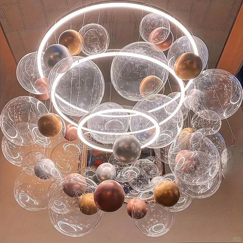A cluster of large clear bubble balloons in various shades of gold, silver, and bronze suspended from the ceiling.