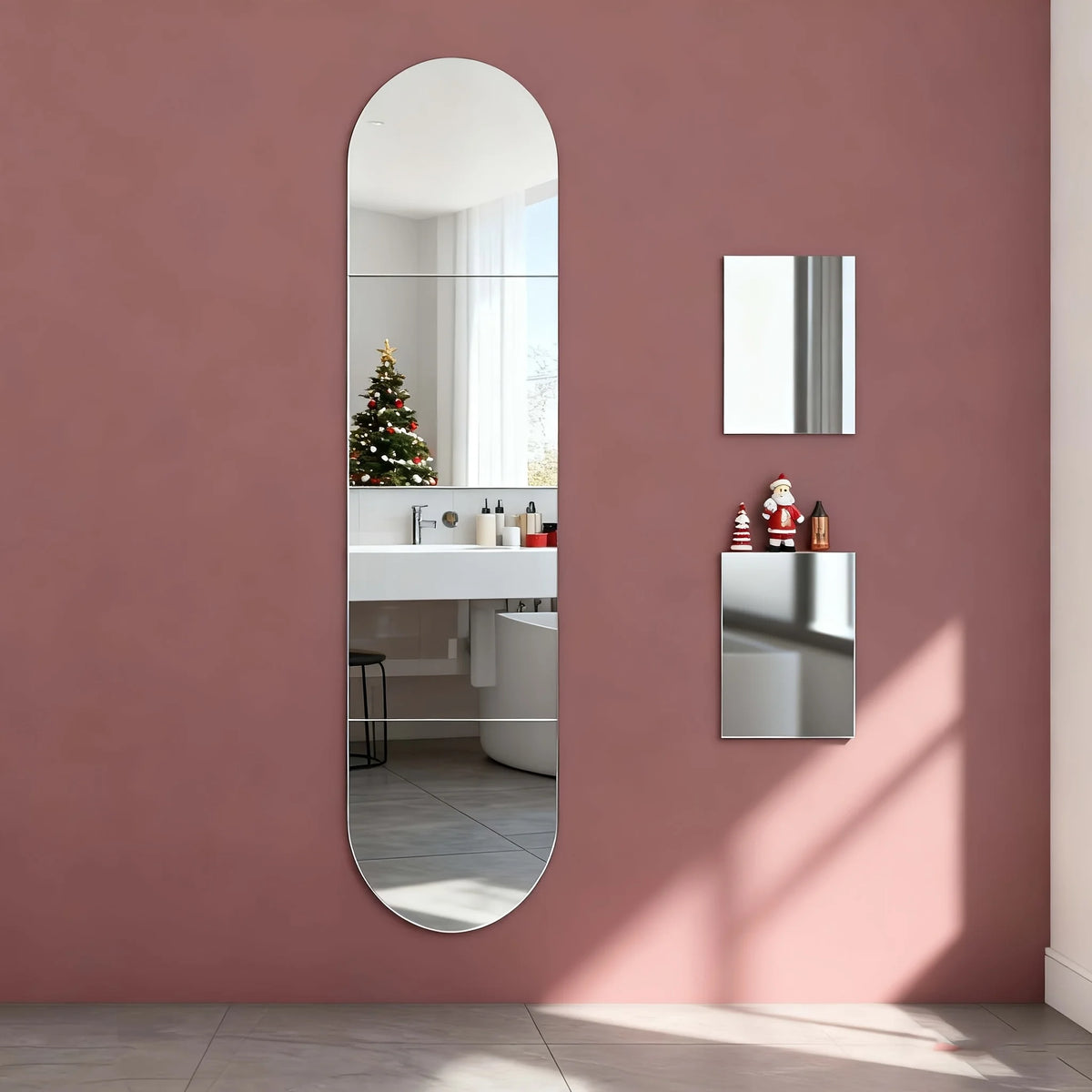 A vertical oval mirror reflects a white shelf with decorative items mounted on a pink wall.