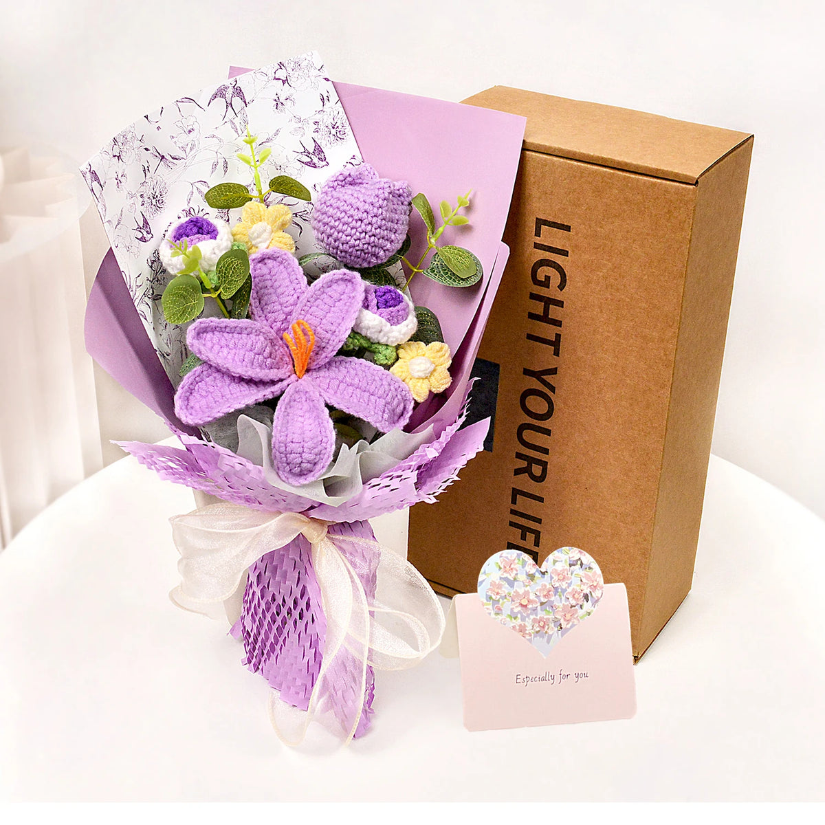 A handmade crochet tulip bouquet in purple and yellow flowers wrapped in lilac paper and presented in a brown gift box.