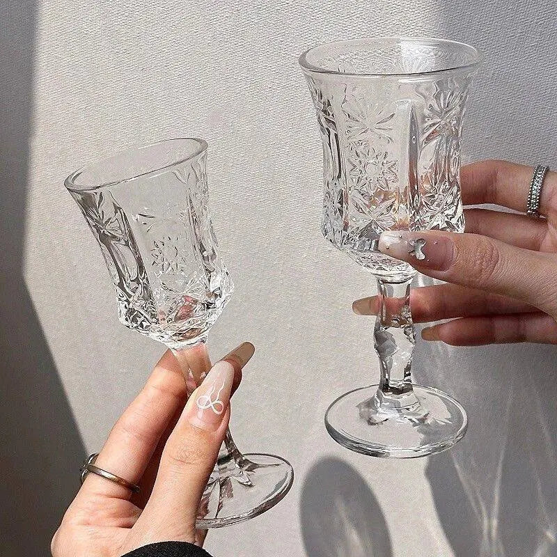 Two vintage French-style high-footed glass wine glasses are held by hands against a light background.