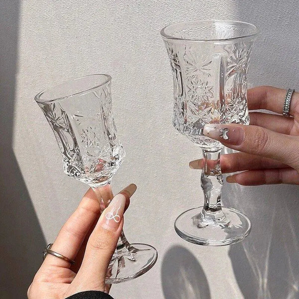 Two vintage French-style high-footed glass wine glasses are held by hands against a light background.