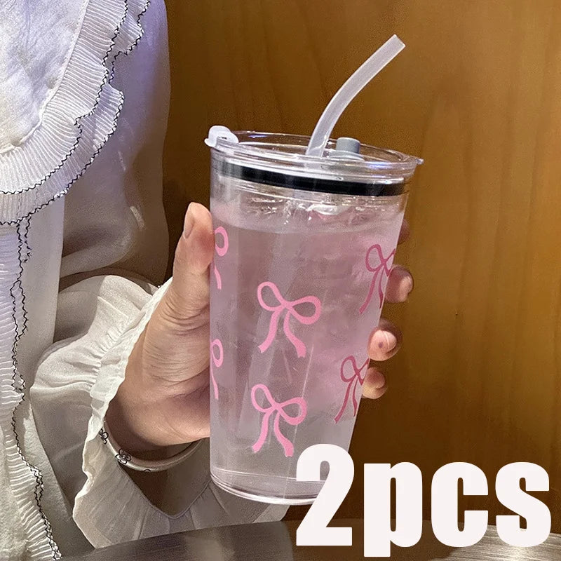 A clear plastic cup with pink bow decorations, a straw, and a lid is held by a person.