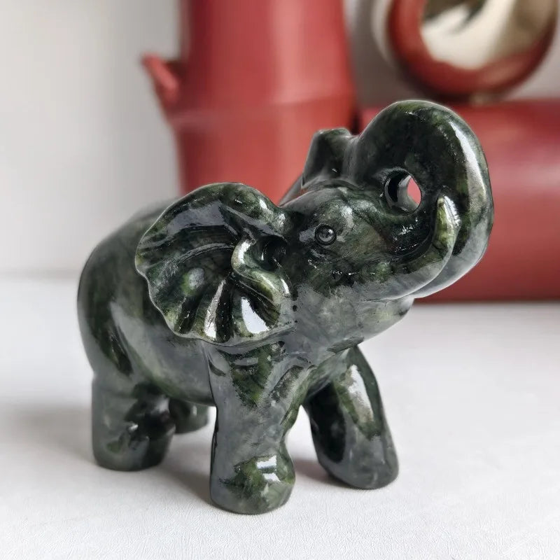 A dark green jade elephant carving statue sitting on a white surface.