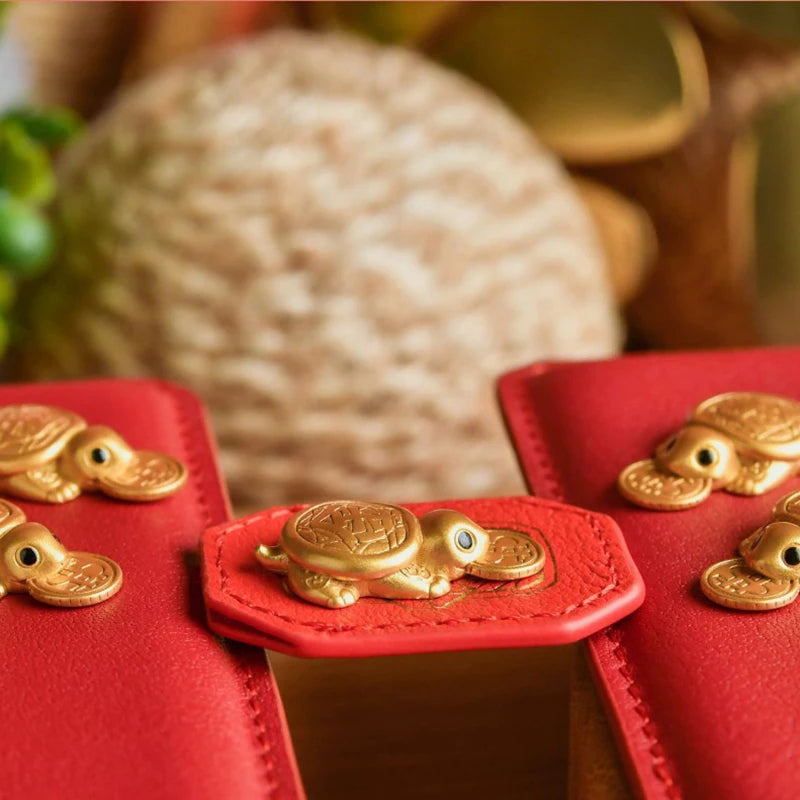 A close-up of a red leather wallet featuring a golden tortoise figurine for wealth luck home decor.
