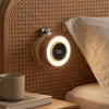 A magnetic bladeless handheld fan with a round light illuminates a textured wall next to a cup and book.