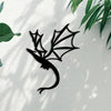 Black metal wall art panel of a dragon silhouette against a light gray wall with dappled shadows.