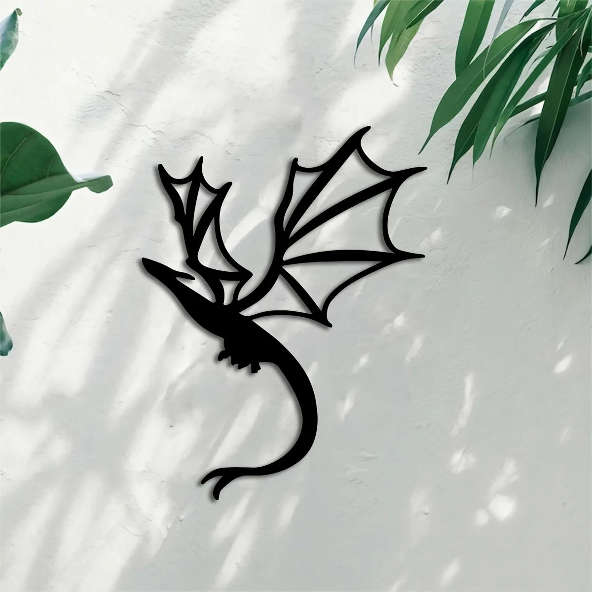 Black metal wall art panel of a dragon silhouette against a light gray wall with dappled shadows.