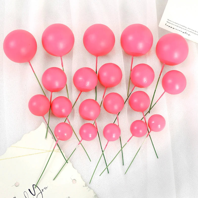 A set of twenty pink spherical ball cake toppers on thin green sticks displayed against a white background.