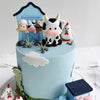 A light blue cake decorated with farm animal toppers including a cow, sheep, and chicken.