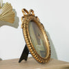 A vintage gold-framed picture frame with a bowknot detail, displaying a portrait, rests on a wooden surface.