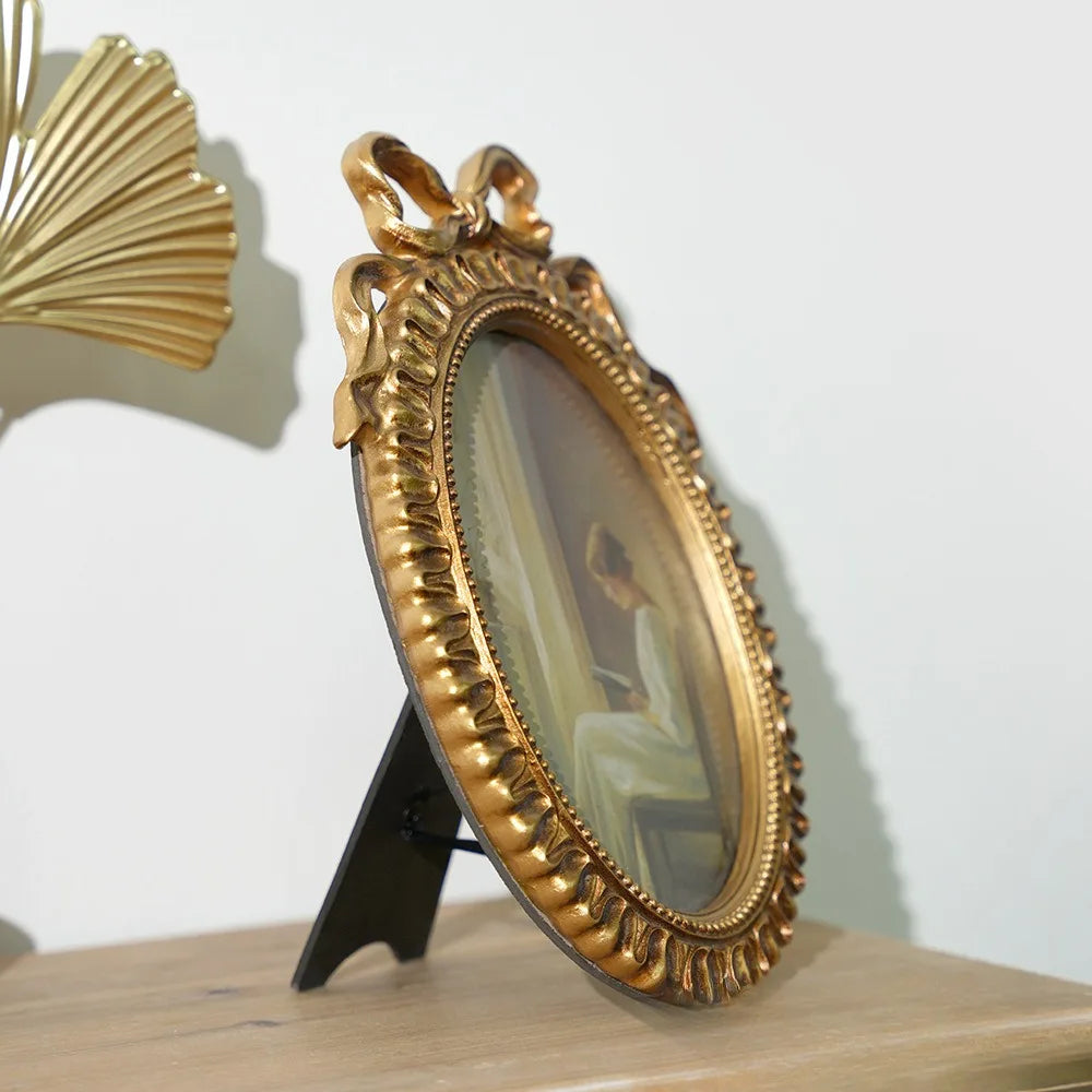 A vintage gold-framed picture frame with a bowknot detail, displaying a portrait, rests on a wooden surface.