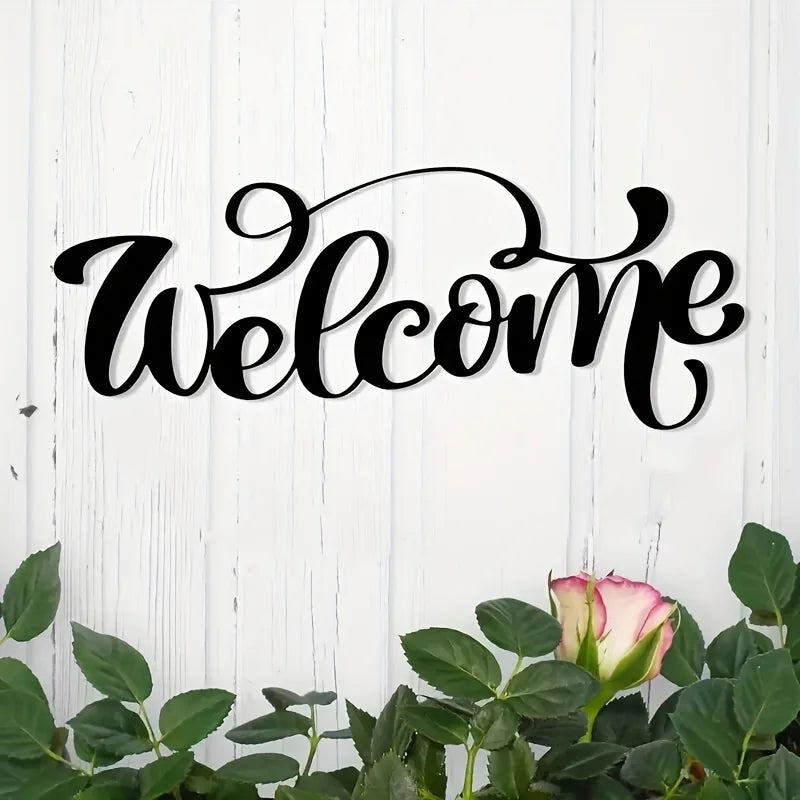 Schwarzer Schrifttext 'Welcome' auf weißem Holz-Hintergrund mit grünem Laub.
