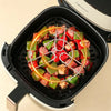 Stainless steel vertical skewer rack with meat and vegetables cooking in an air fryer basket