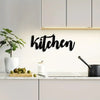 Black script wall art spelling 'kitchen' mounted on a white kitchen backsplash
