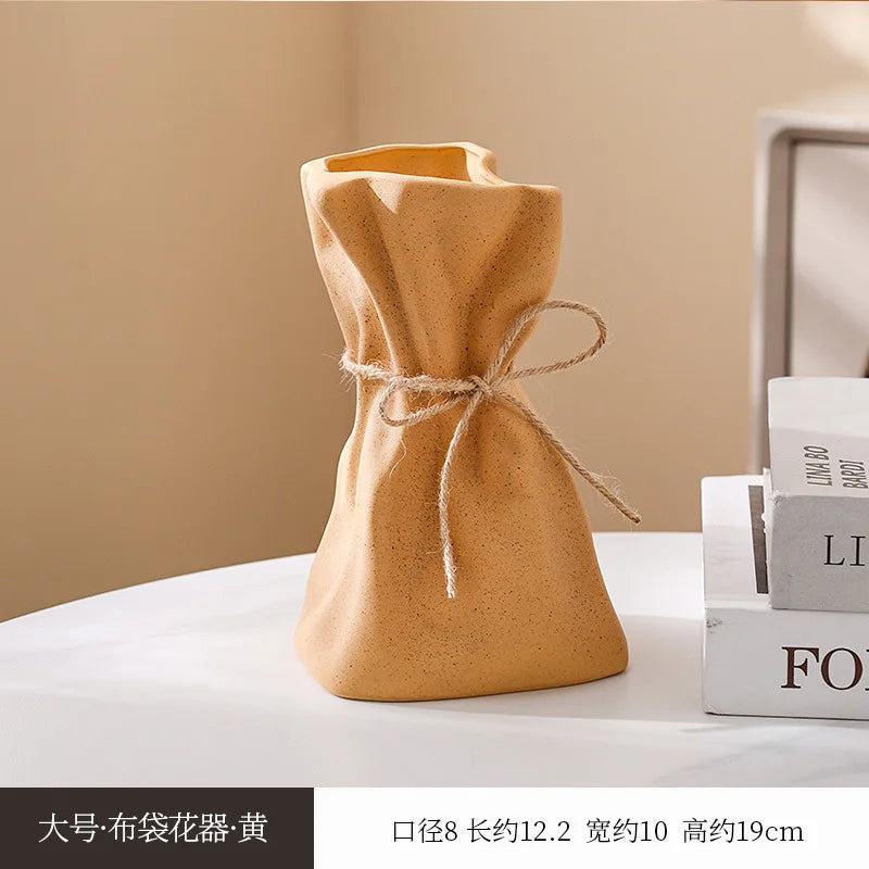 A small, mustard-colored ceramic money bag shaped vase with a twine tie, displayed on a white surface.