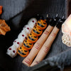 A collection of Halloween skull and skeleton aromatherapy candles in various orange and white designs resting on dark fabric.
