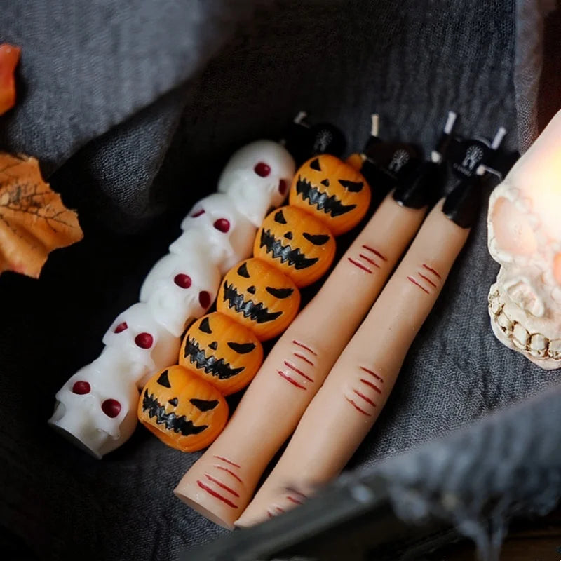 A collection of Halloween skull and skeleton aromatherapy candles in various orange and white designs resting on dark fabric.