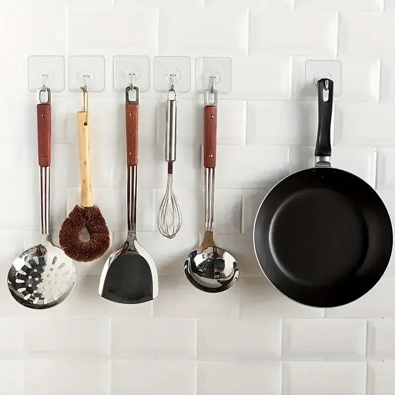 A row of transparent self-adhesive wall hooks displaying various kitchen utensils hanging from them.