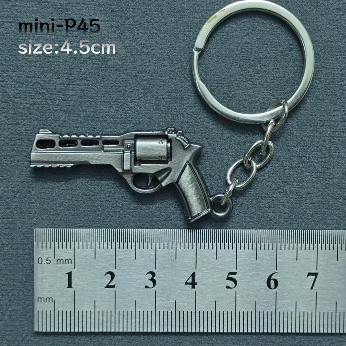 A silver miniature P45 pistol model attached to a metal keyring, measured against a ruler.