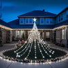 A Christmas tree made of white lights stands in a garden setting with a starry topper and surrounding lights.