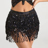 A woman wearing a black sequin skirt with tassel belts and a cropped top.