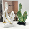 White and green feather sculptures displayed on a black base next to a book.