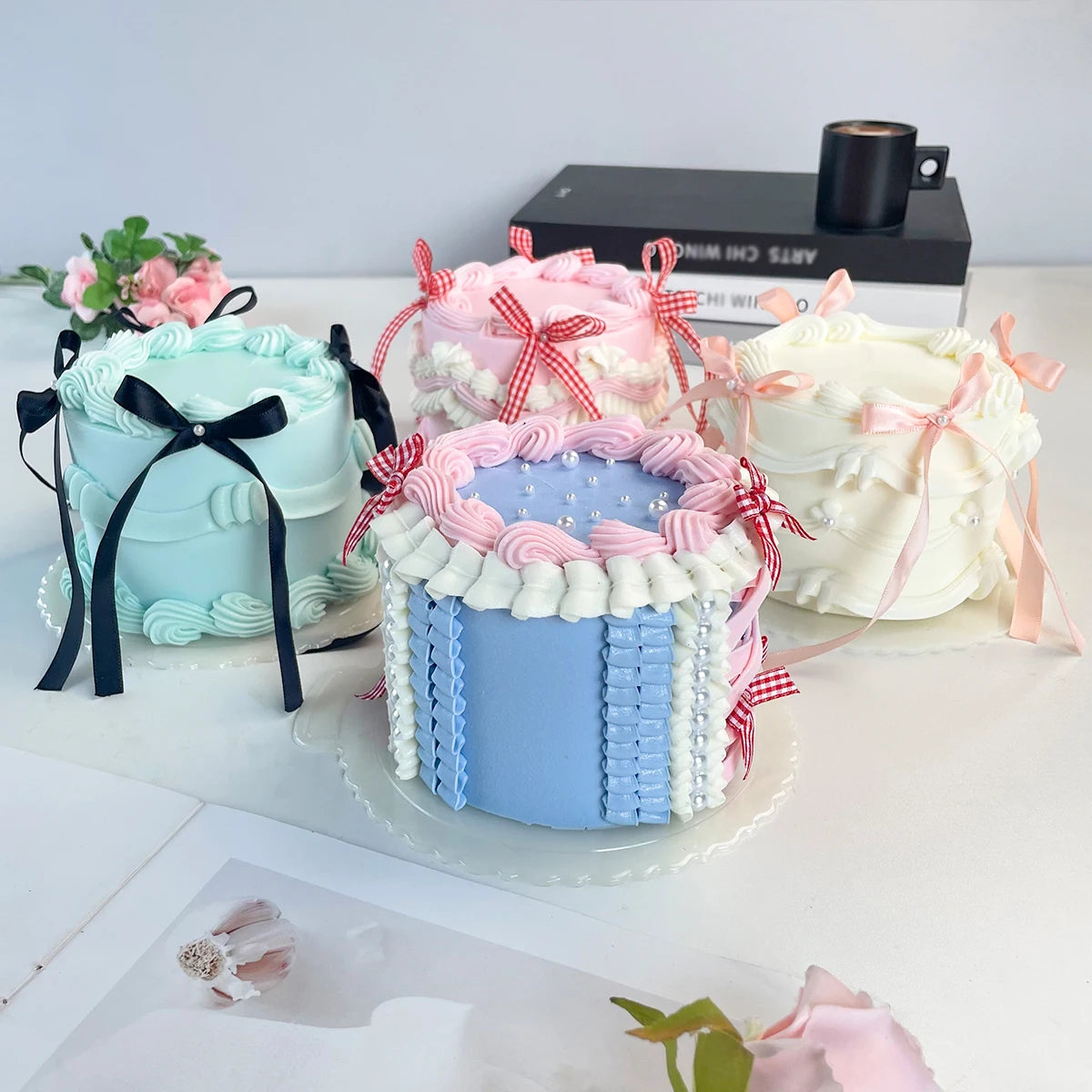 A display of four decorative fake cakes in various pastel colors, including blue, pink, and white.