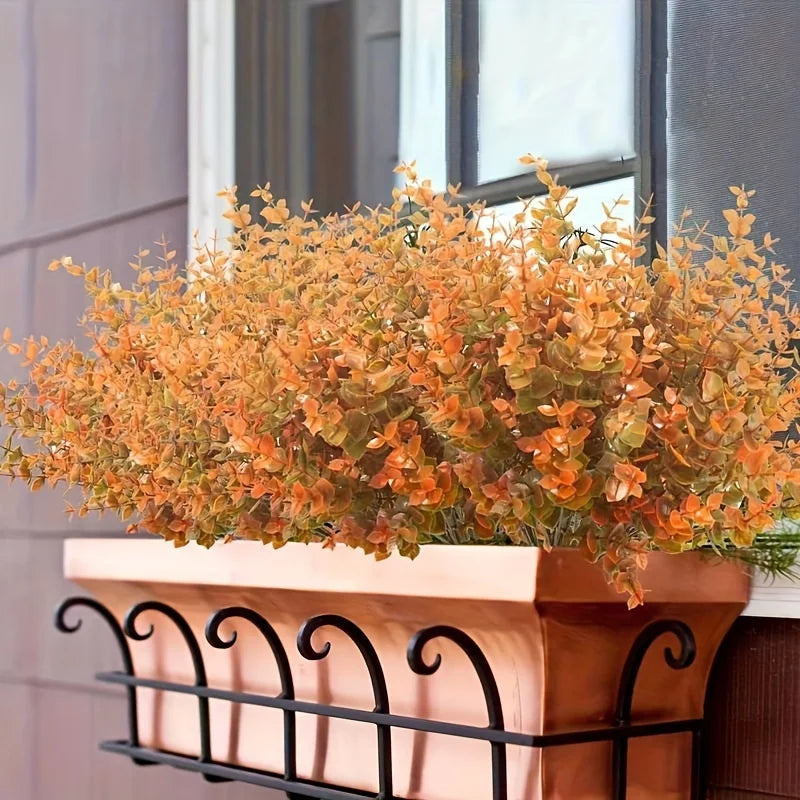 A bouquet of artificial orange and yellow fall flowers in a terracotta planter