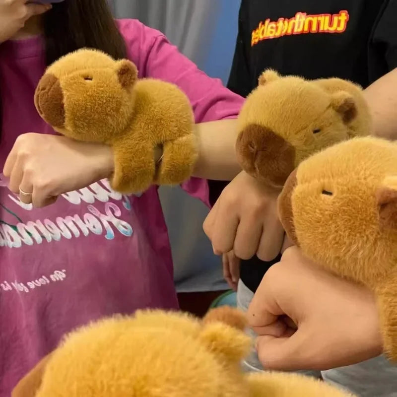 Several people are holding or displaying fluffy golden capybara animal wristbands and rings.