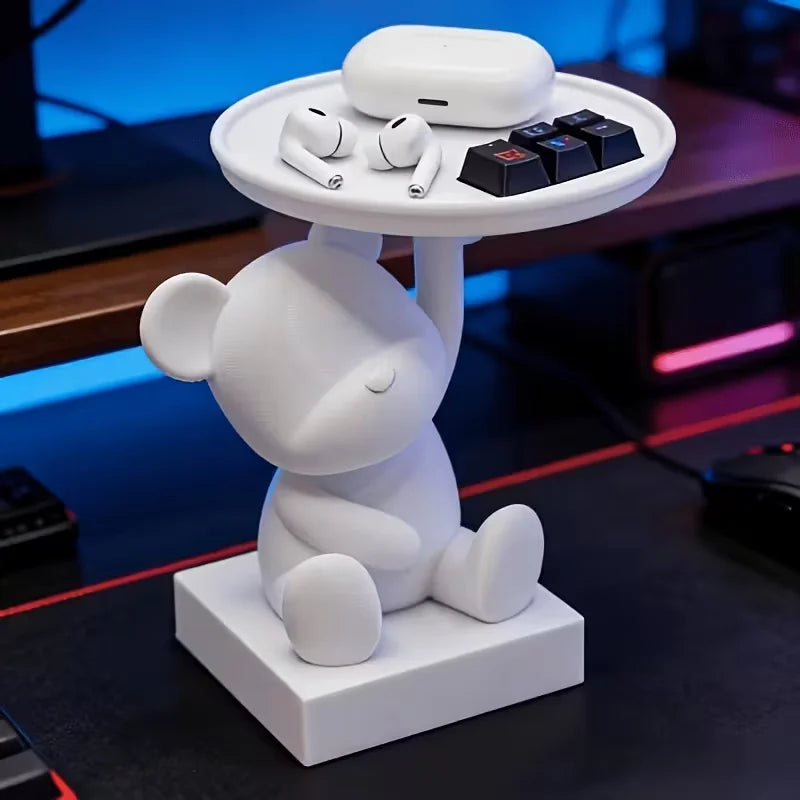 A white bear-shaped tray holds a pair of headphones and several small accessories on a dark surface.