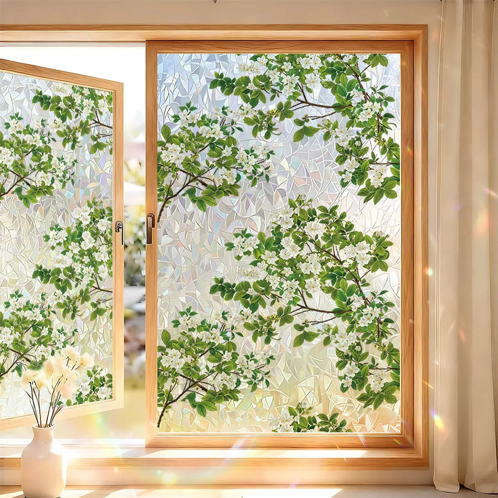 A close-up view of a window with decorative privacy film featuring green leaves and white blossoms.