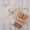 A beige fabric pouch tied with twine holds wooden baby milestone cards marked for 12 months.