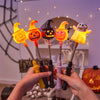 Une main tient une canne de lanterne d'Halloween orange lumineuse avec un motif de citrouille sculptée sur un arrière-plan fl